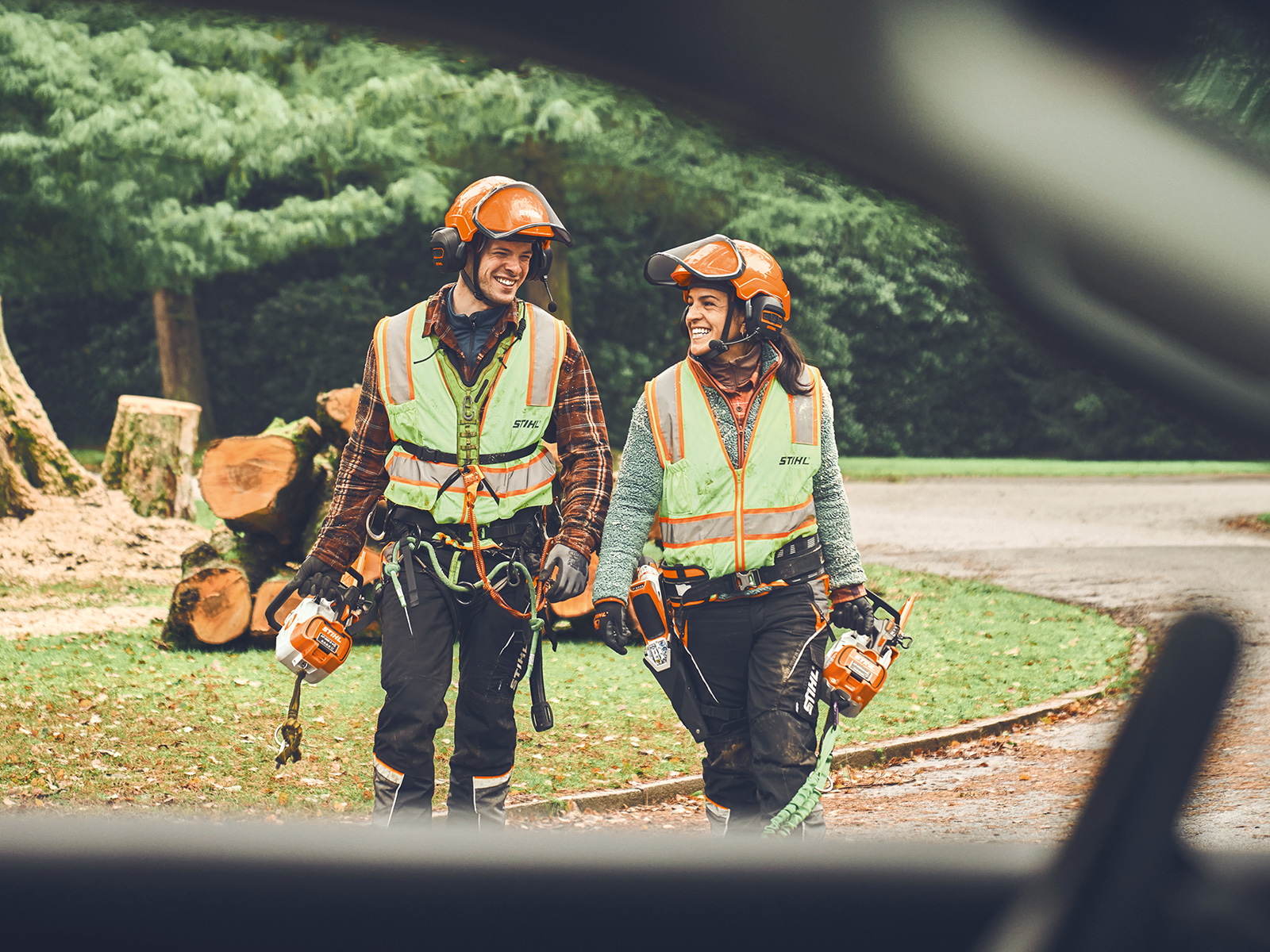 A man and a woman with STIHL cordless chainsaws and a STIHL cordless pruner walk smiling towards a car  